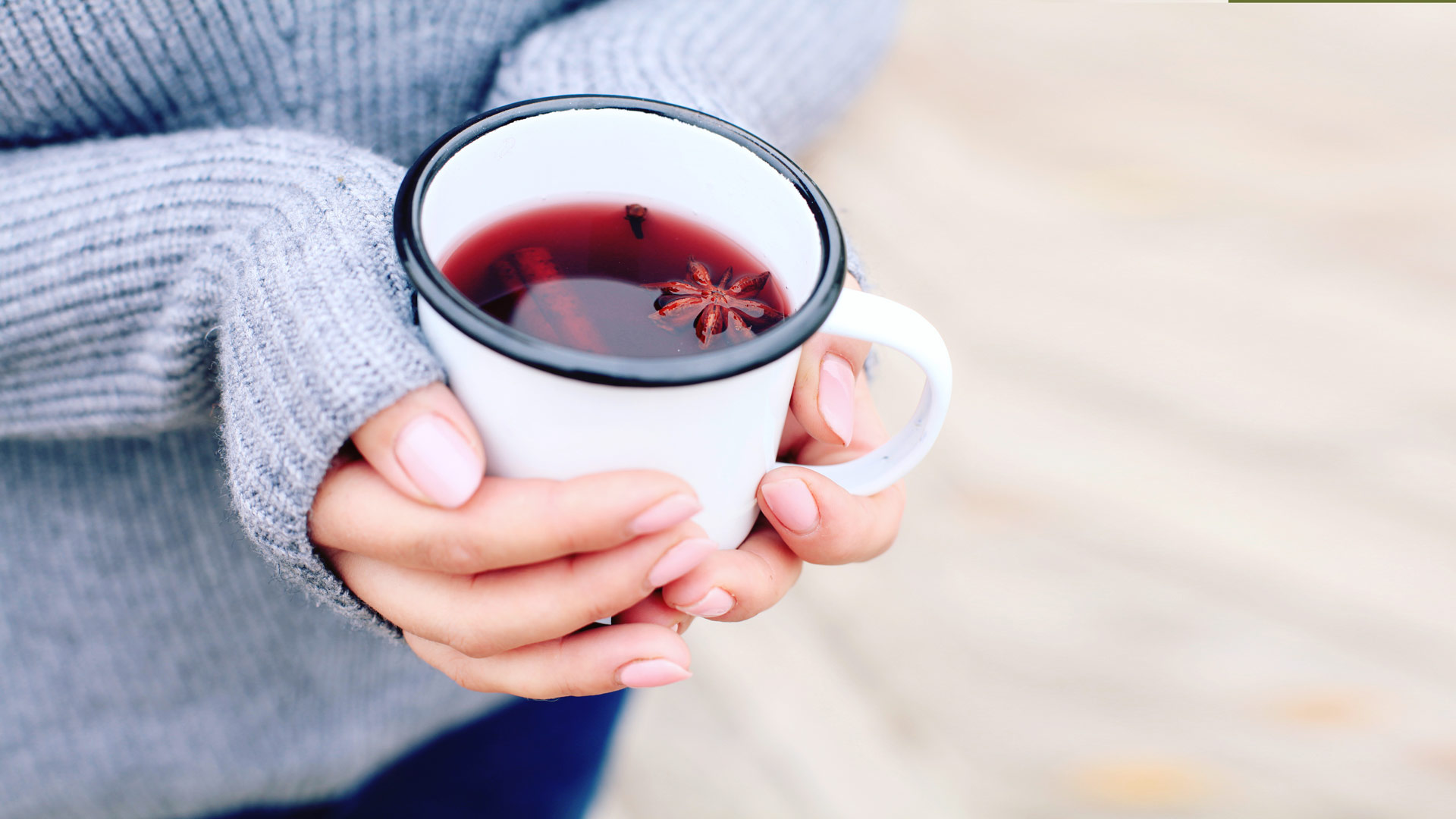 Hände halten eine weiße Tasse mit rotem Getränk und Sternanis.