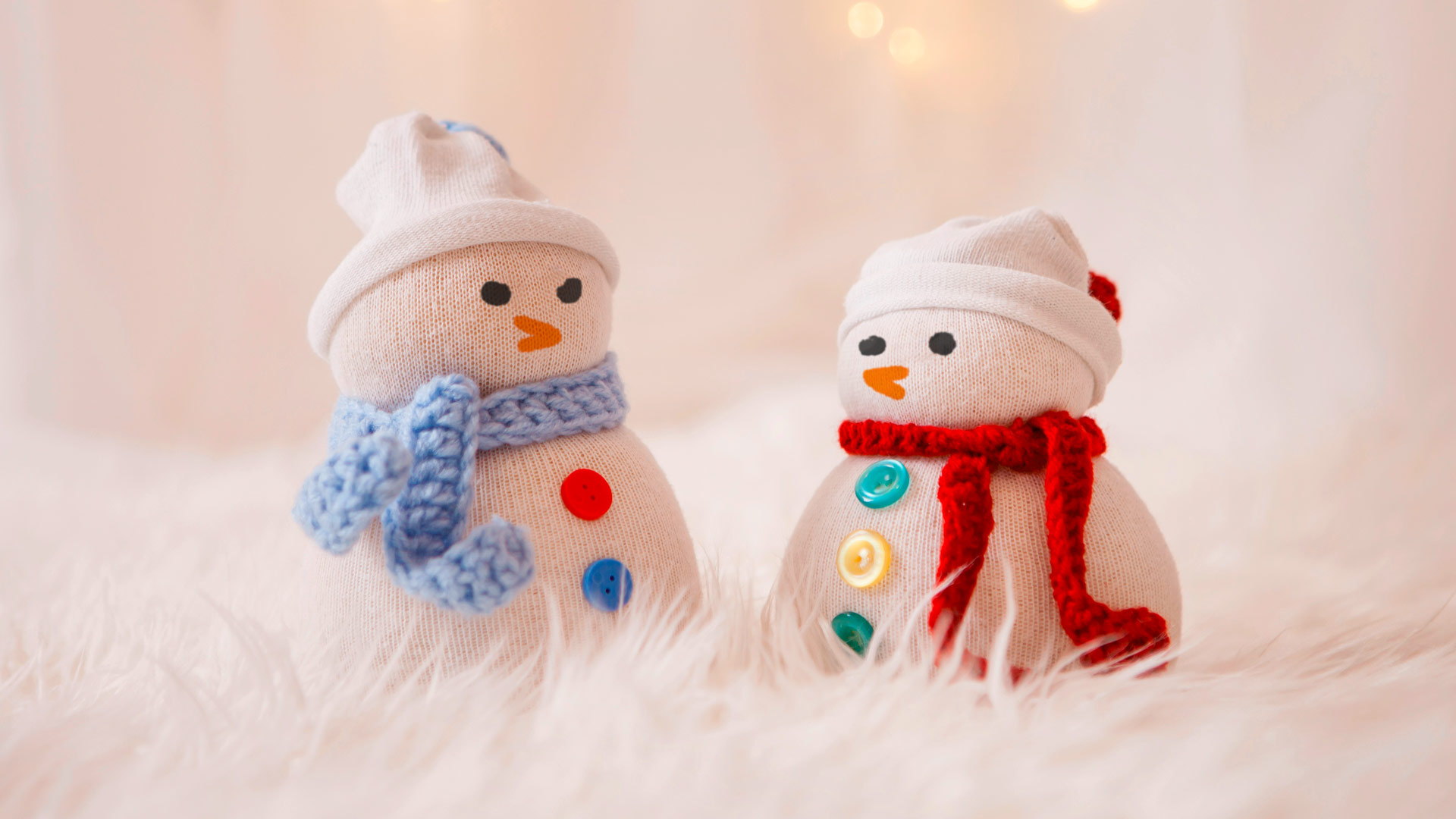 Zwei gestrickte Schneemänner mit Schal und Knöpfen stehen vor weißem Hintergrund.