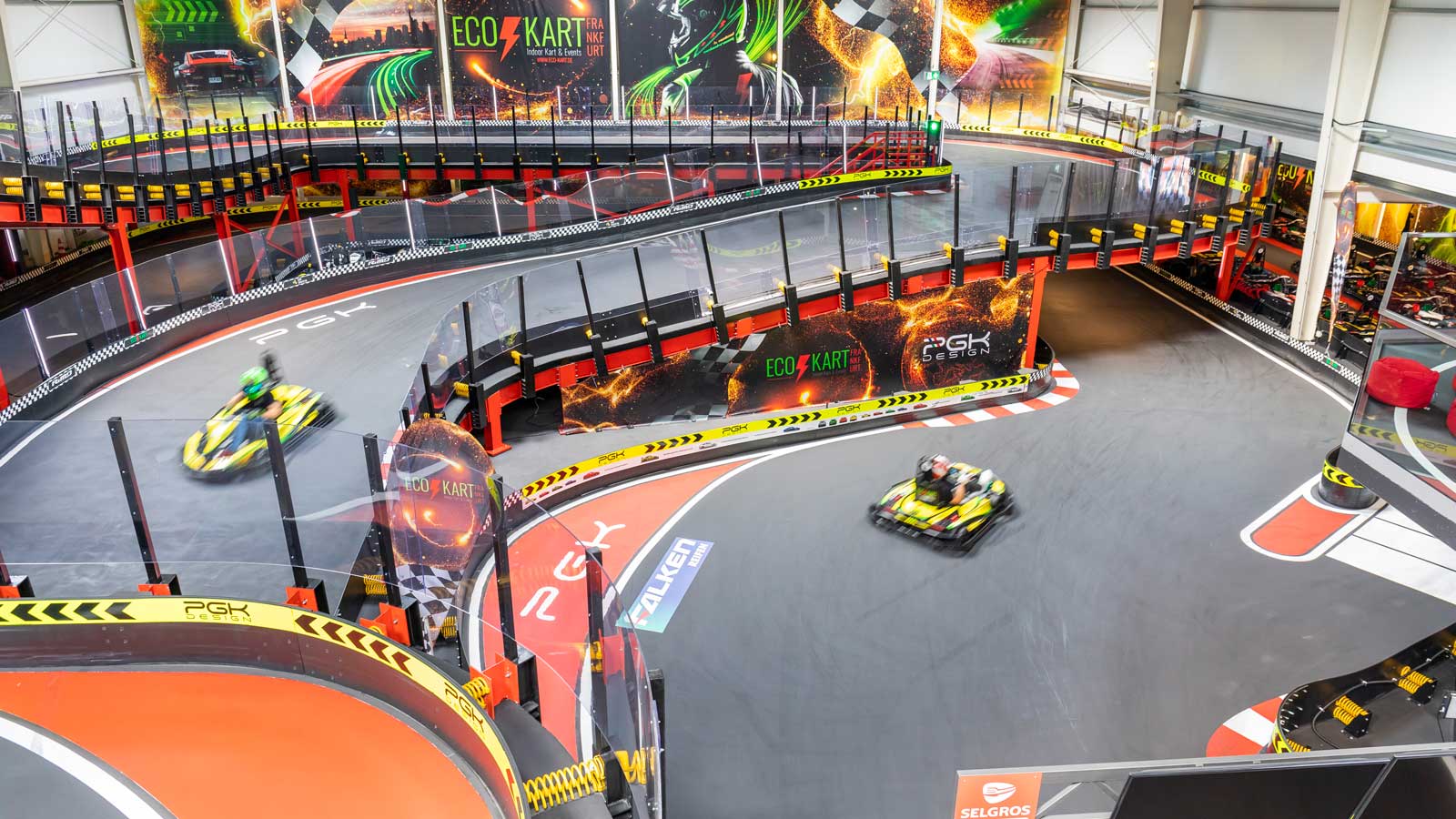 Kartrennen in einer Indoor-Halle mit mehreren Fahrzeugen auf einer blauen Rennstrecke.