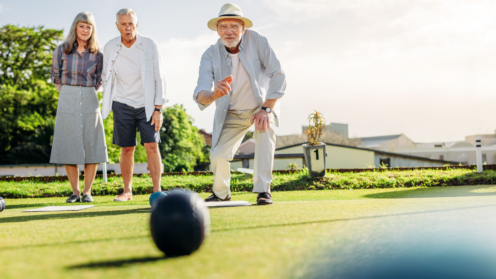 Zwei Seniorinnen und ein Senior spielen Boule auf Rasen.