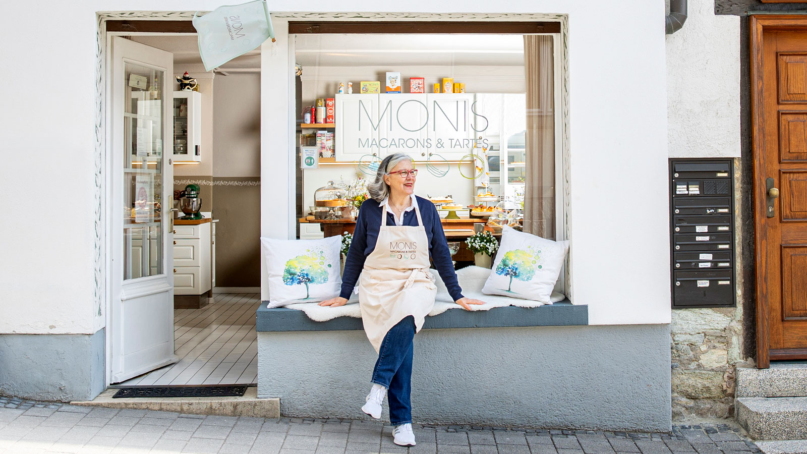 Frau in Schürze vor Laden mit Aufschrift 'Macarons & Tartes'