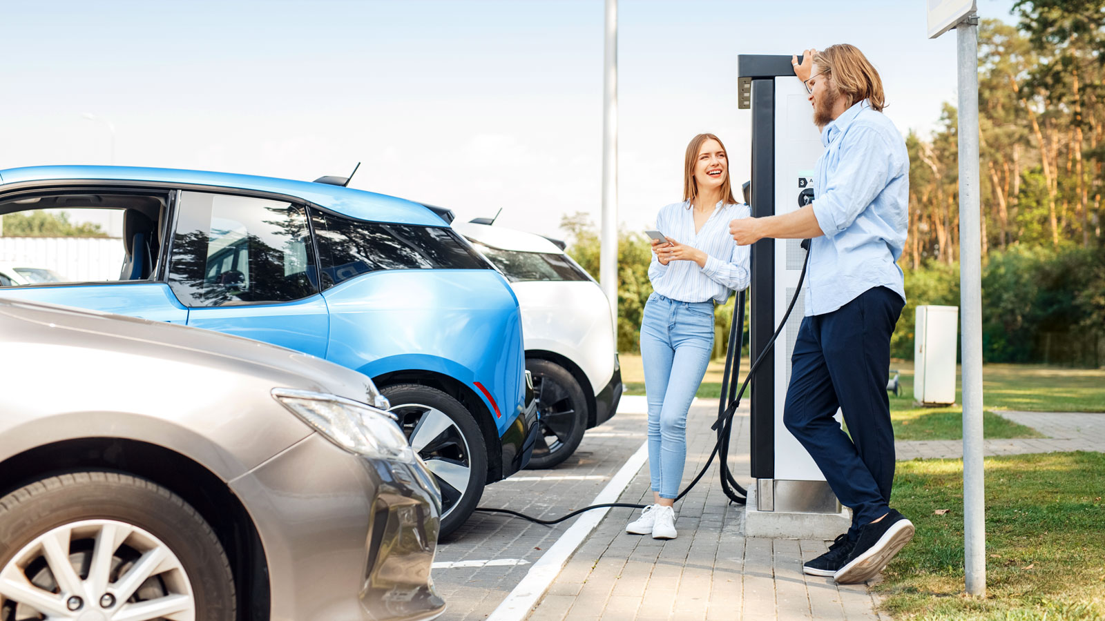 Zwei Personen laden Elektroautos an einer Ladestation.