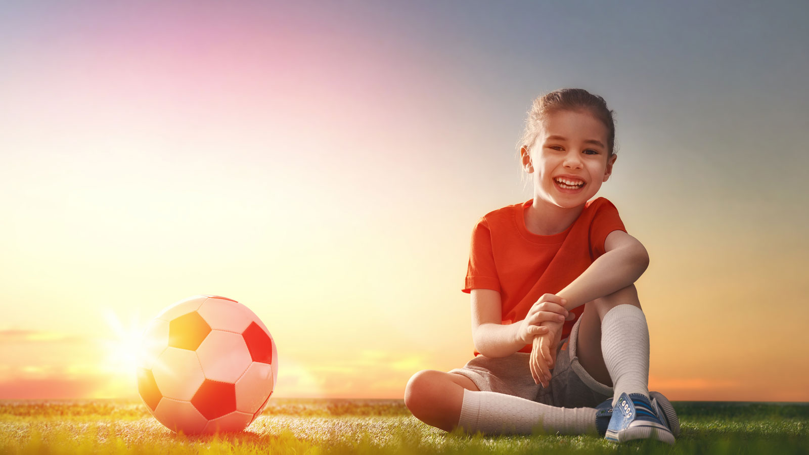 Mädchen sitzt auf Gras, hält Fußball