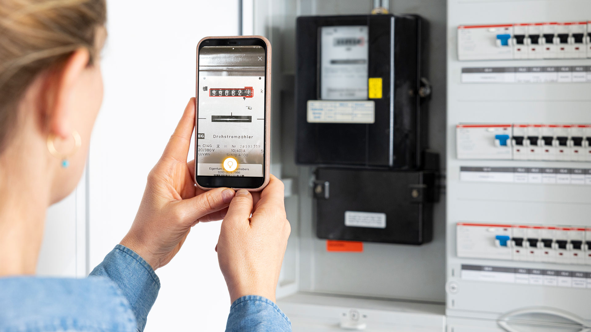 Person fotografiert Stromzähler mit Smartphone.