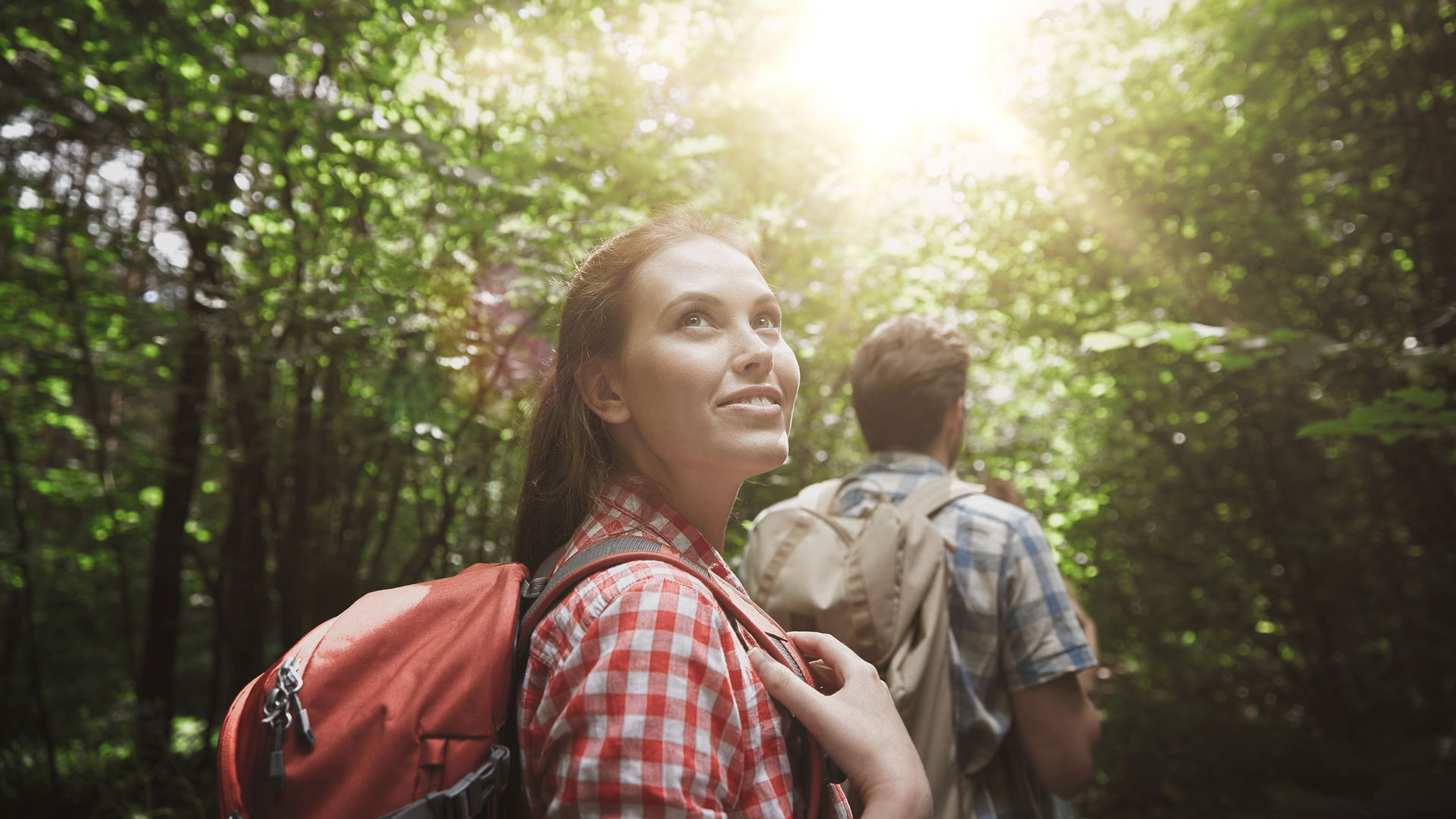 Zwei Wanderer mit Rucksäcken im Wald, Blick nach oben.