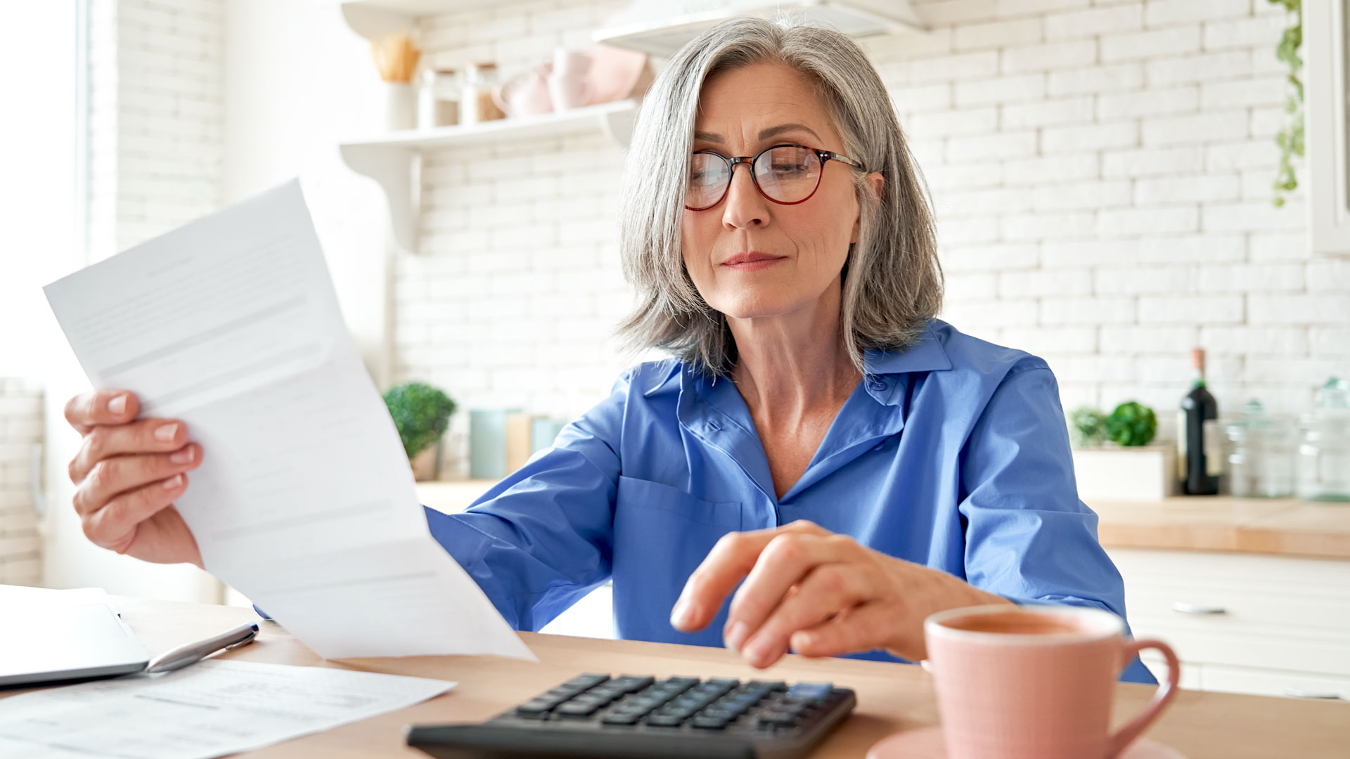 Frau liest Dokument am Küchentisch.