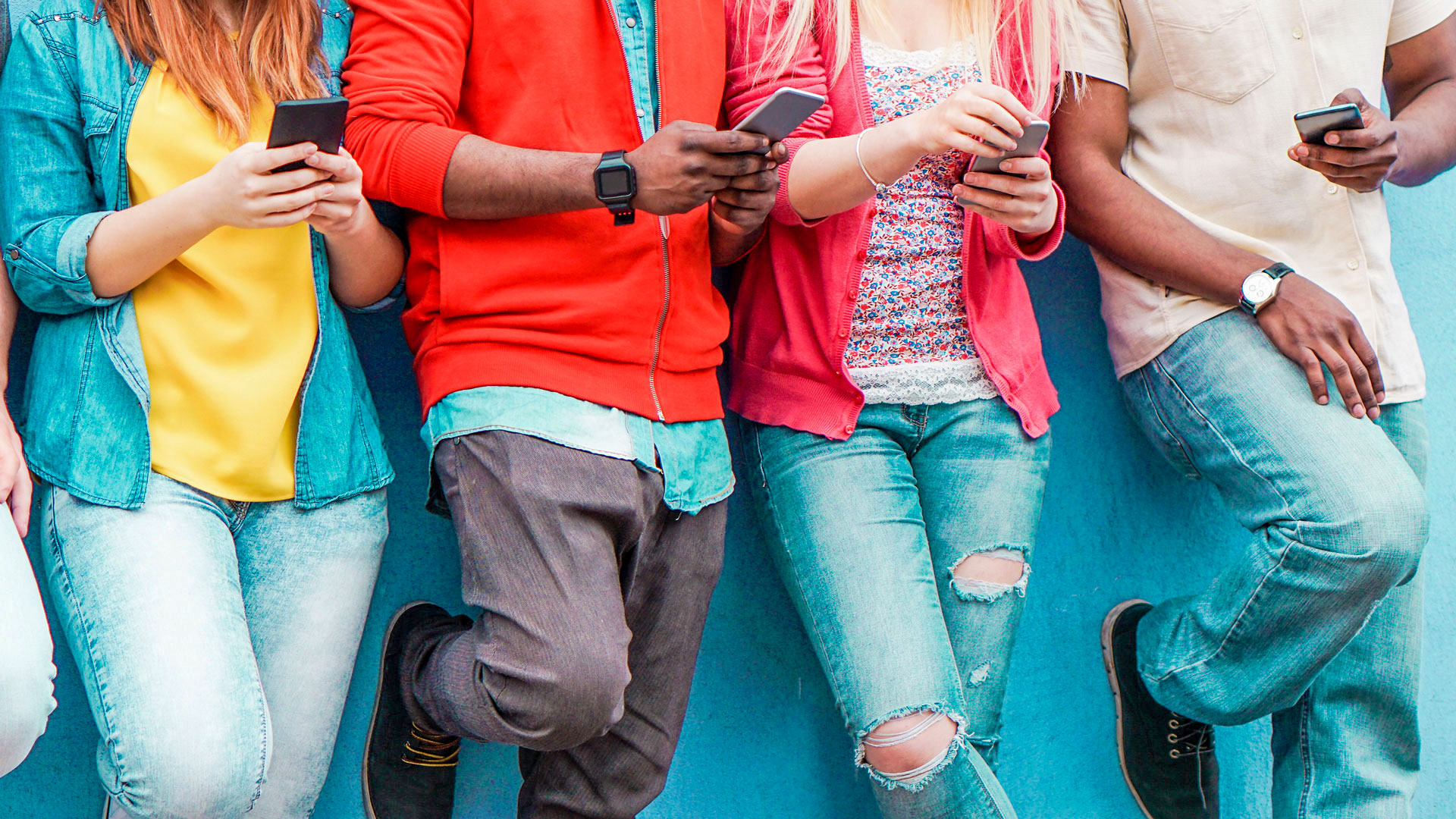 Vier Personen mit Smartphones, alle tragen Jeans und bunte Oberteile.