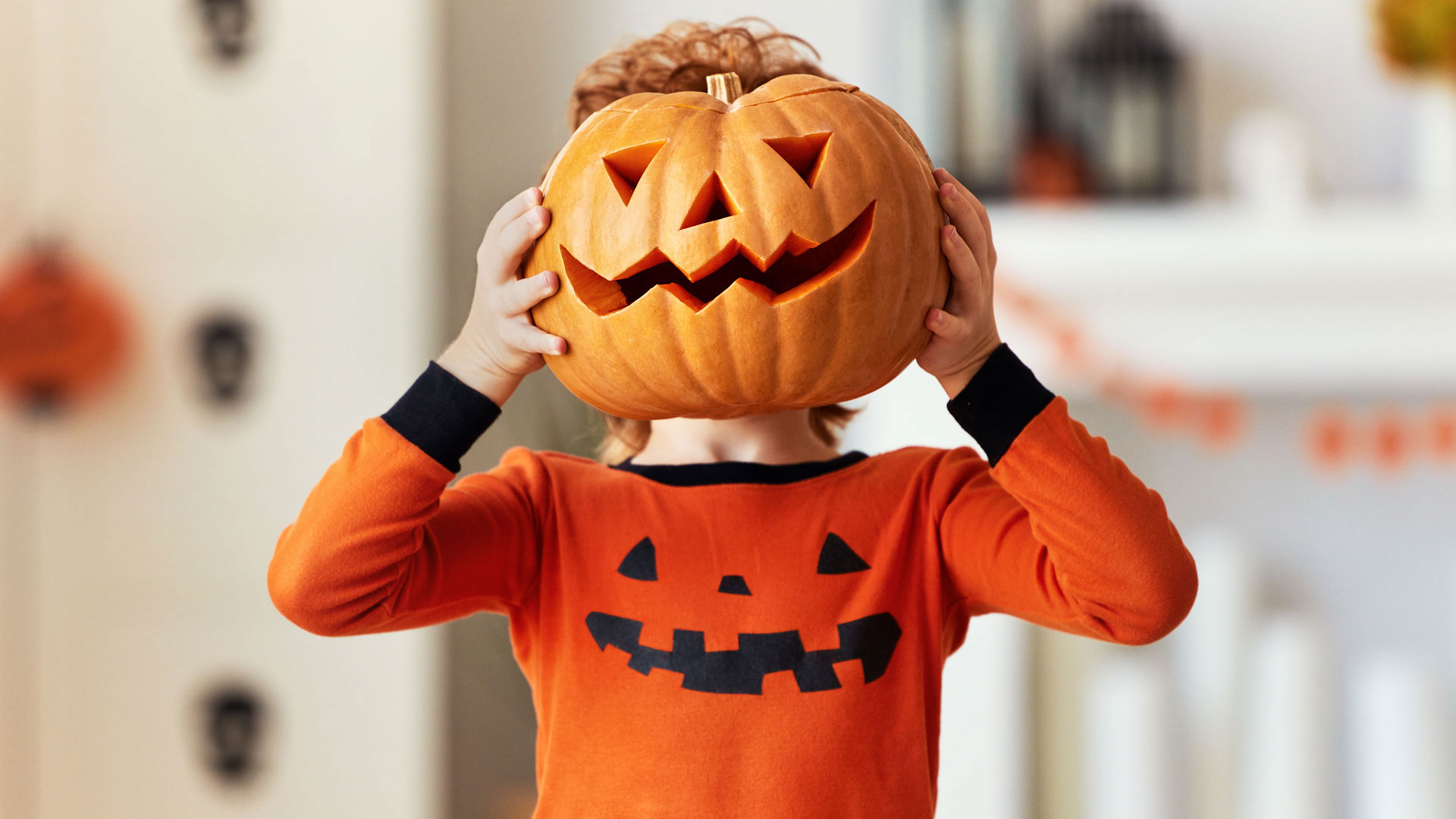 Kind mit geschnitztem Kürbis vor dem Gesicht
