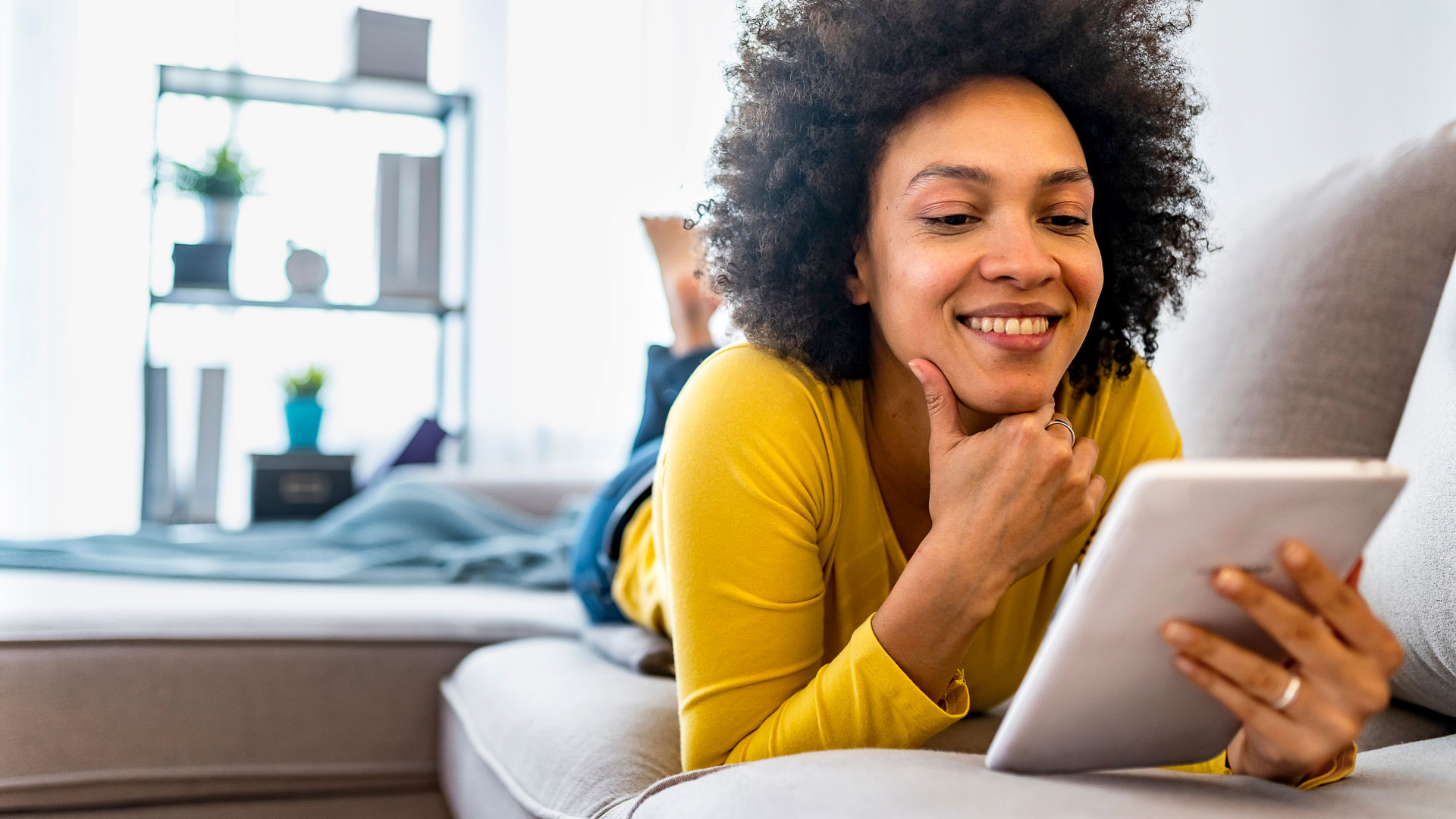 Frau mit gelocktem Haar lächelt und hält ein Tablet.