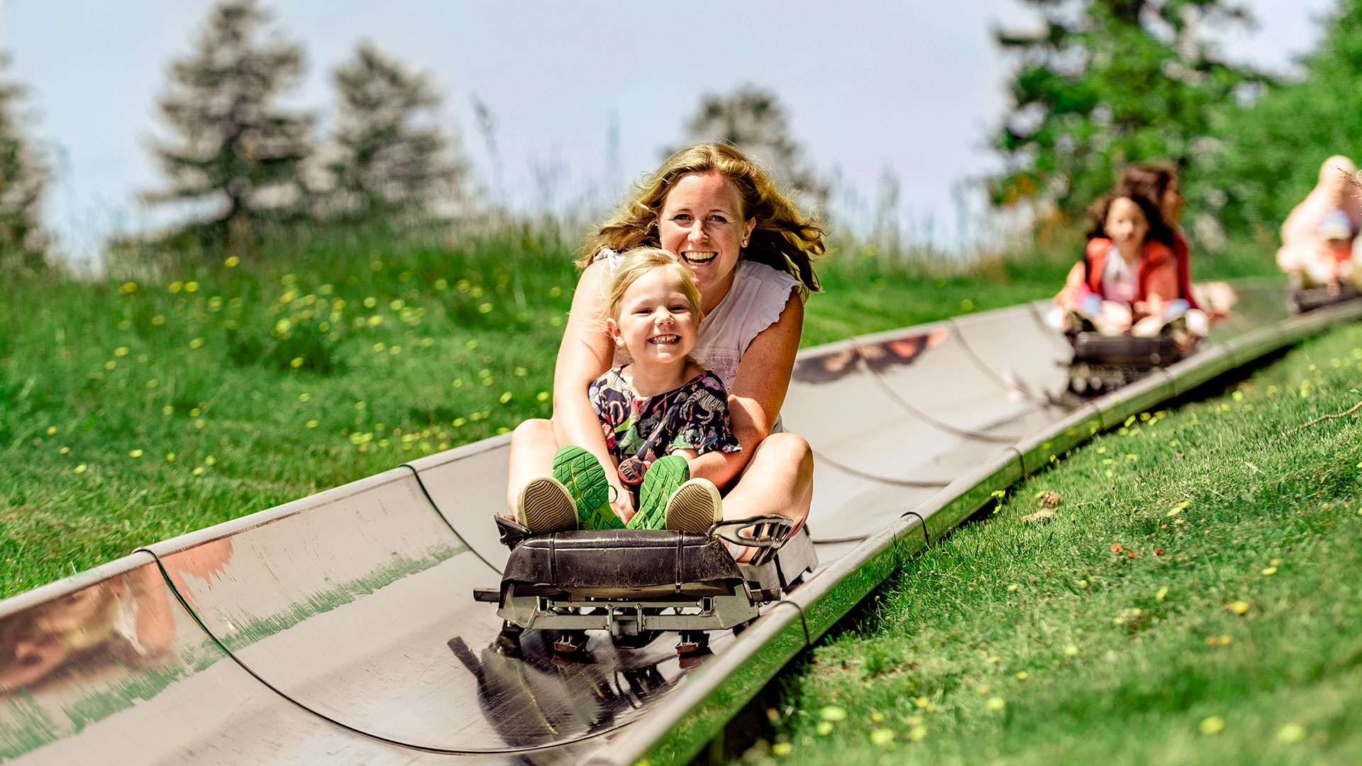 Zwei Kinder fahren auf einer Sommerrodelbahn bergab.