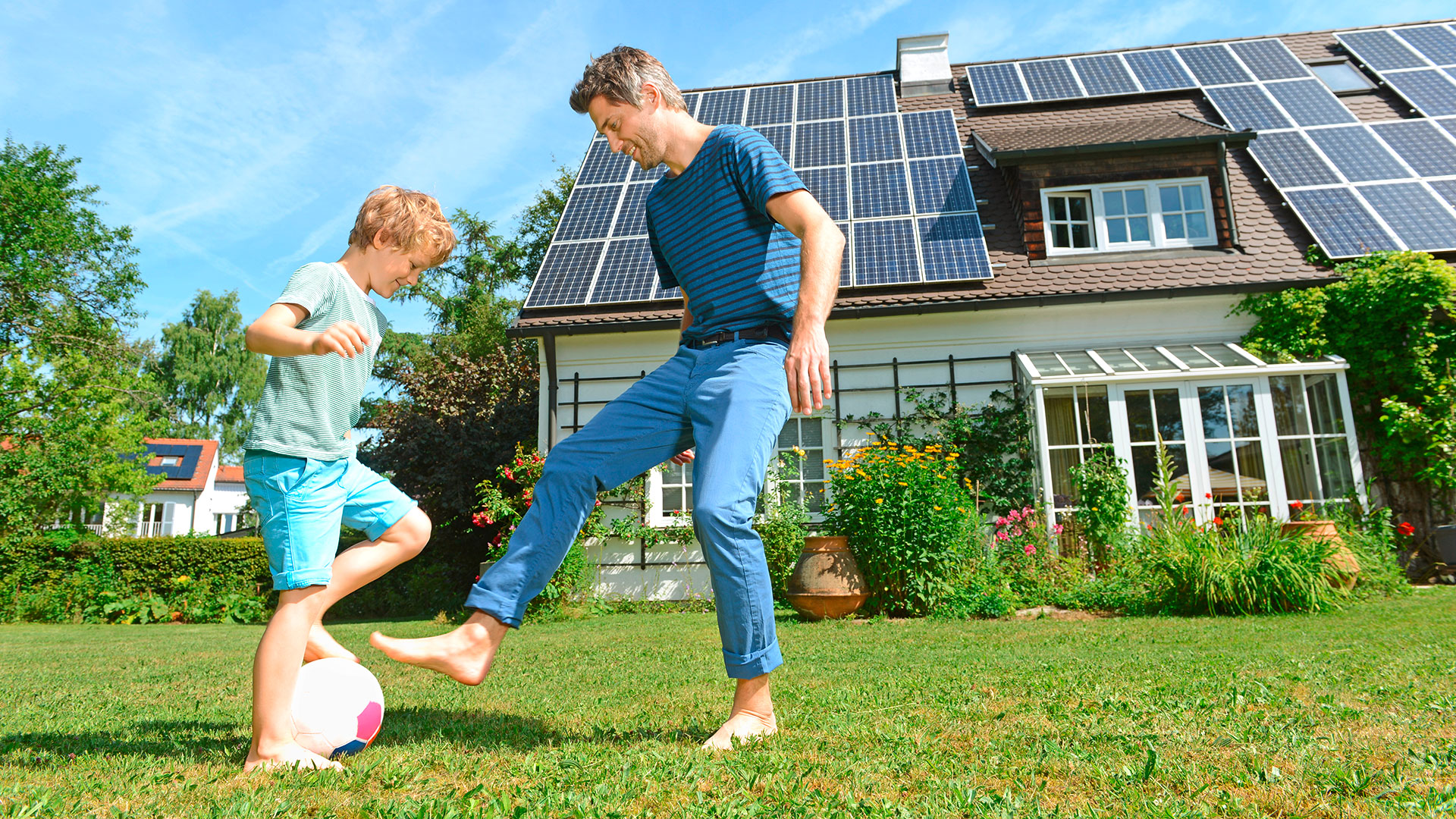 Mann und Kind spielen Fußball vor einem Haus mit Solaranlage.
