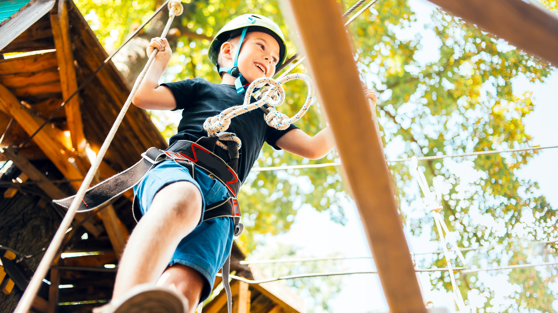Junge klettert mit Helm und Sicherung im Kletterwald.