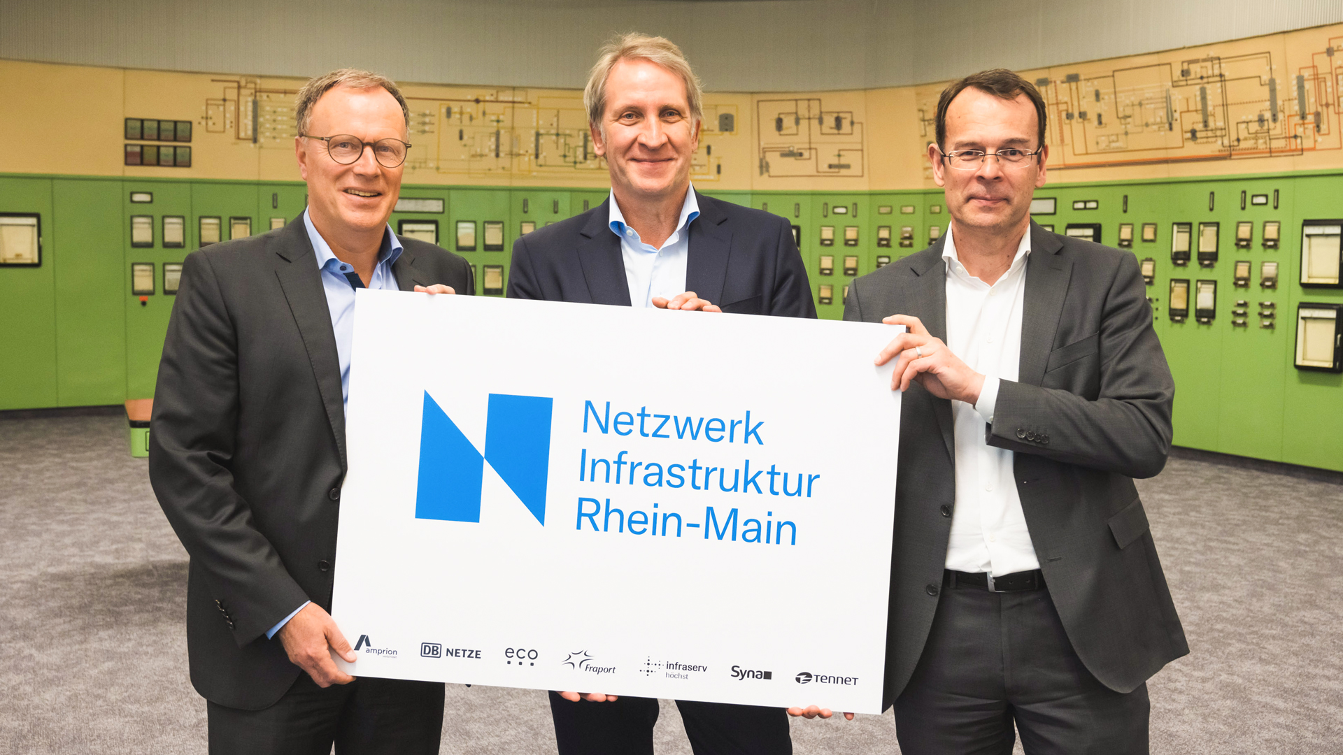 Drei Männer in Anzügen halten ein Schild mit dem Aufdruck 'Netzwerk Infrastruktur Rhein-Main'