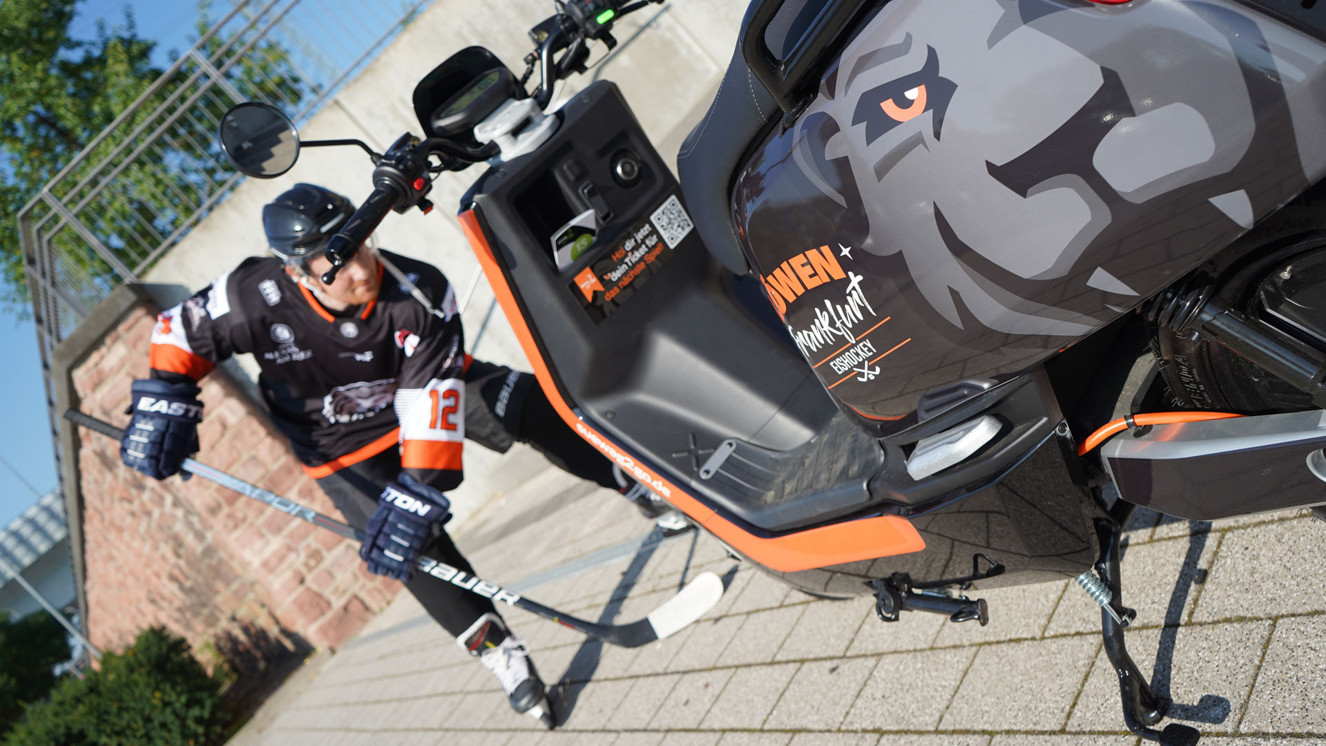 E-Roller mit Seitenwagen, beschriftet mit 'E-Hero' und 'Wie ein Star'. Rechts ein Sportler in Ausrüstung.