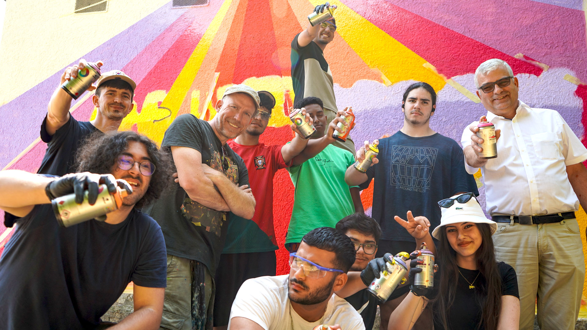Gruppe von Menschen mit Spraydosen vor farbenfroher Wand.