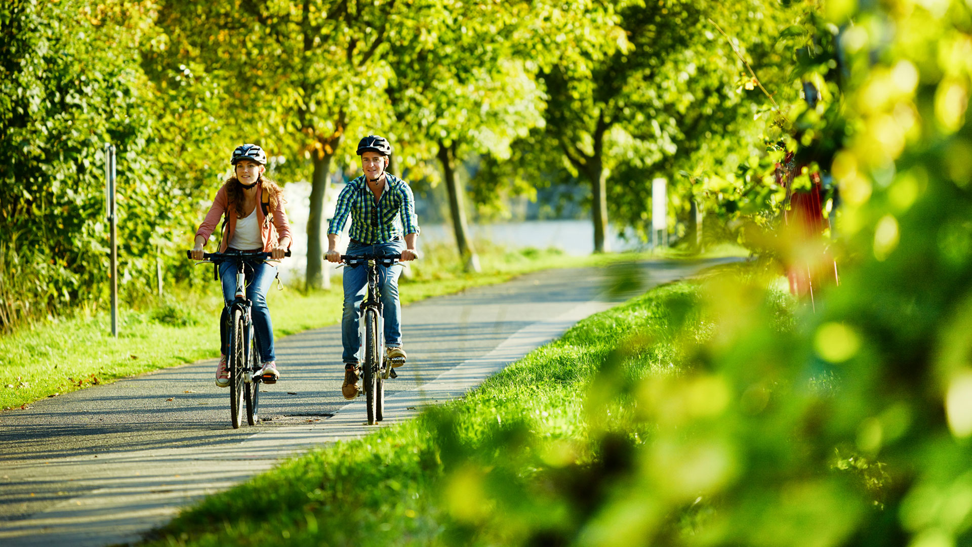 Zwei Radfahrer auf einem befestigten Weg durch eine grüne Landschaft.