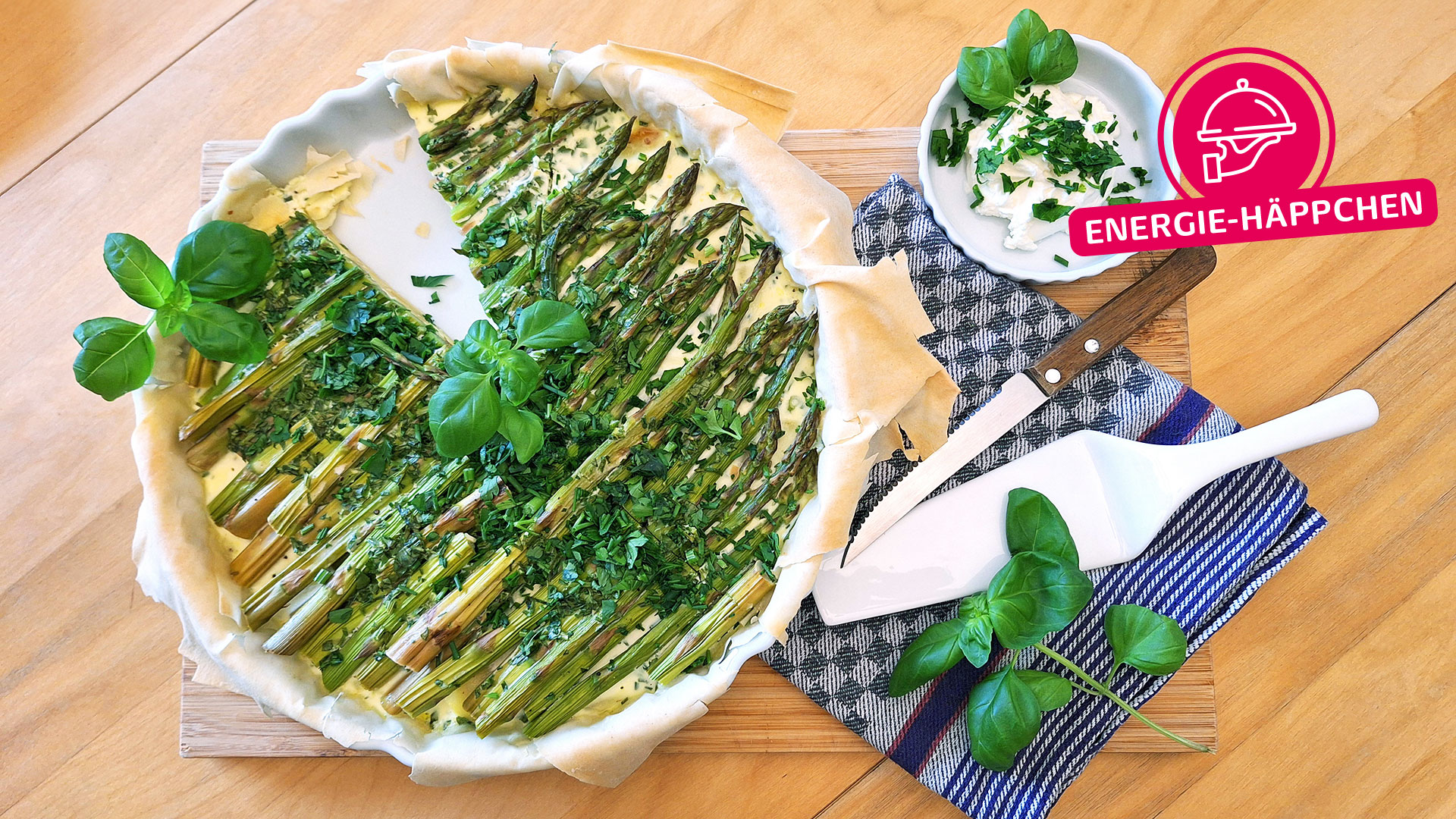 Spargelquiche mit frischen Kräutern und einem Stück Käsekuchen daneben.
