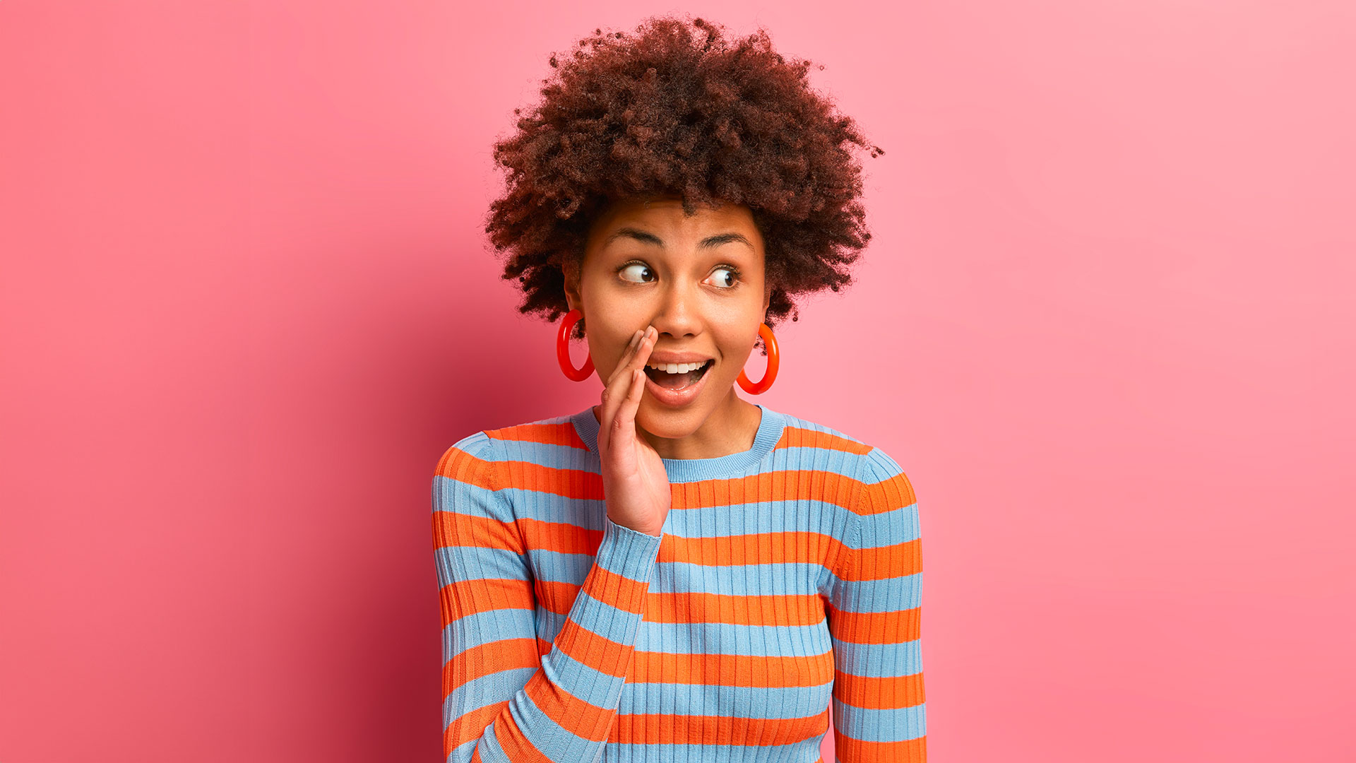 Frau mit gelocktem Haar flüstert in die Hand.