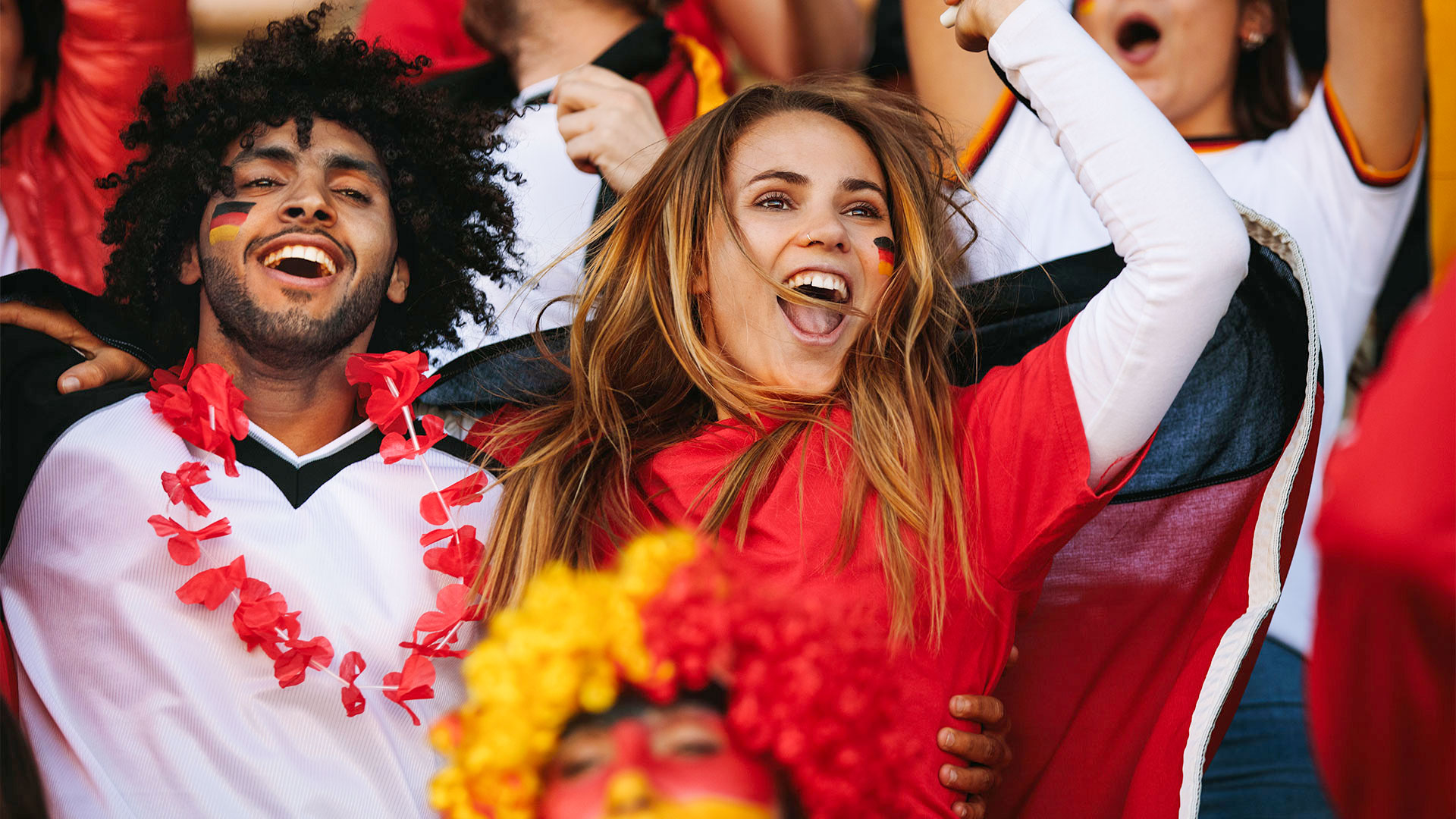 Zwei jubelnde Personen mit Deutschlandfahnen und Gesichtsbemalung.