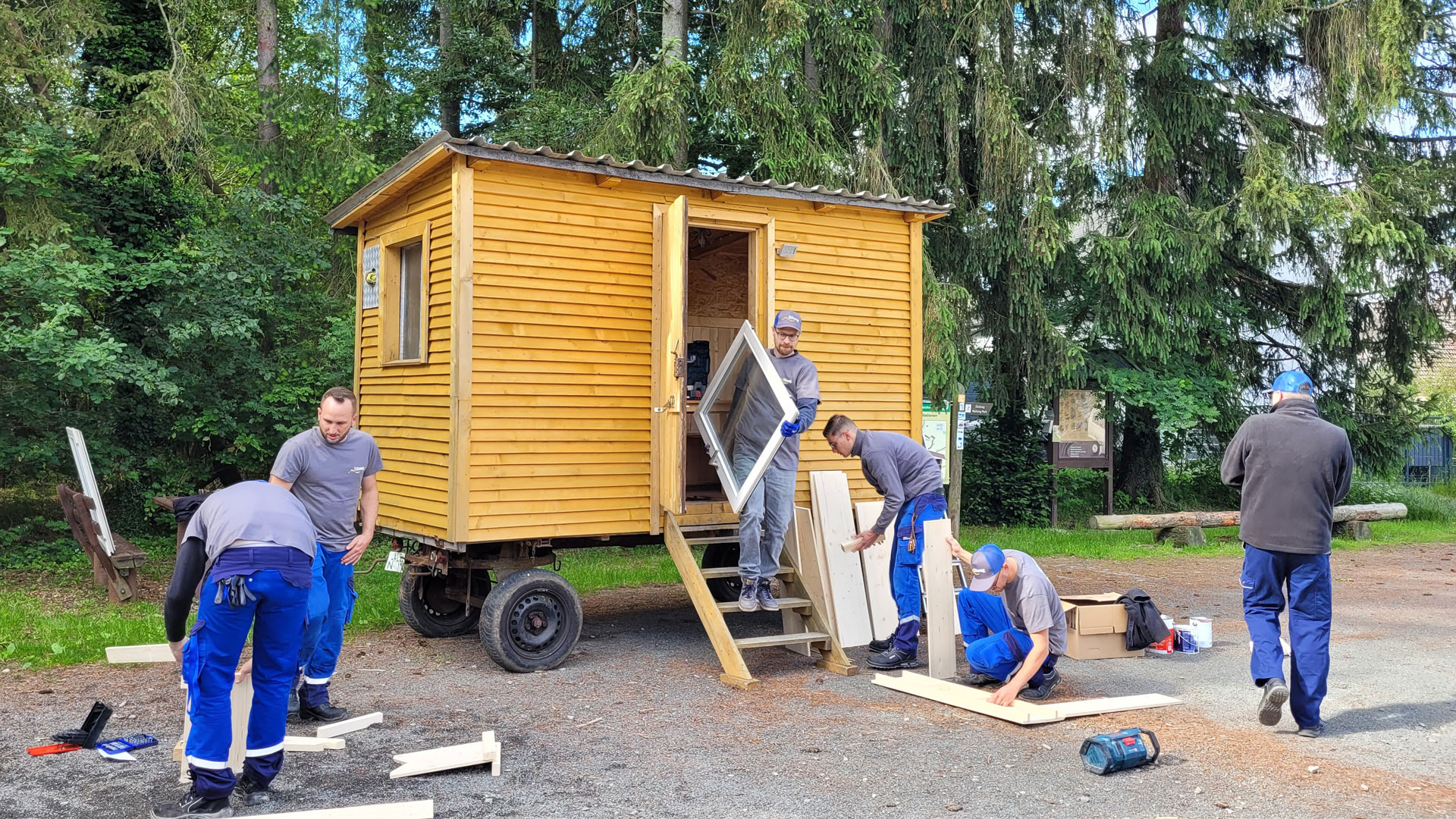Drei Handwerker montieren eine Holzverkleidung an einem mobilen Holzhaus.