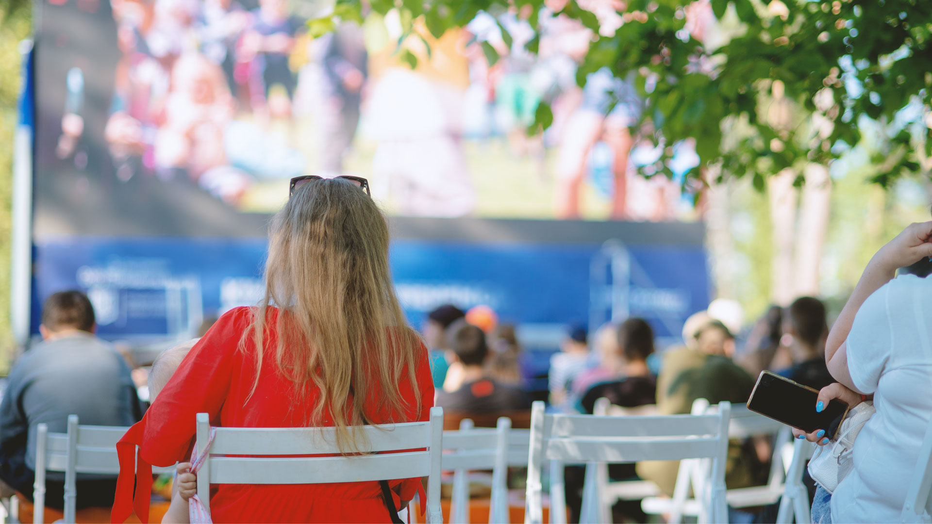 Zuschauer bei einer Open-Air-Kino-Veranstaltung, Blick auf die Rückenlehnen der Stühle und den Bildschirm.