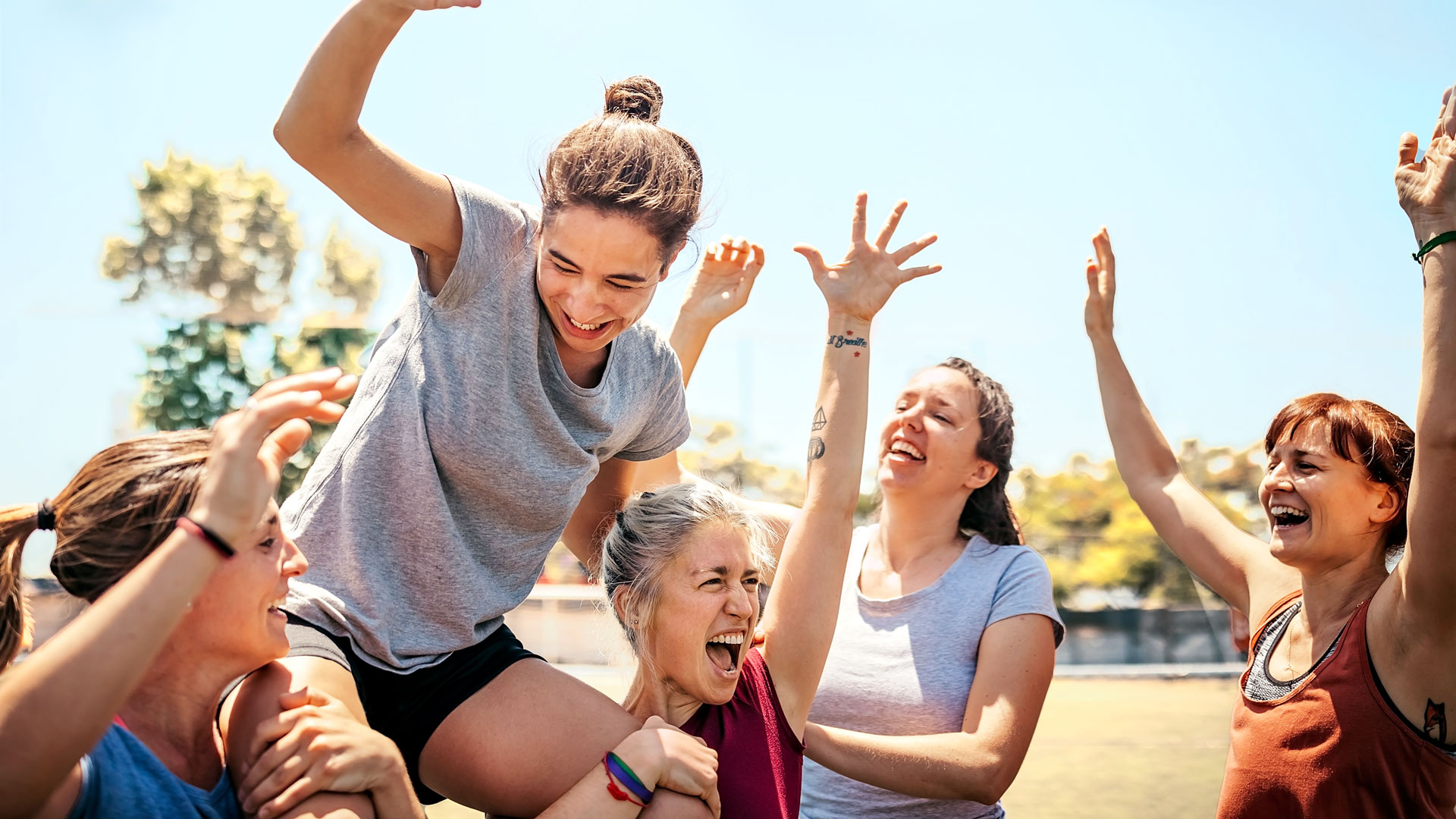 Gruppe lachender Frauen, eine hebt eine andere hoch.