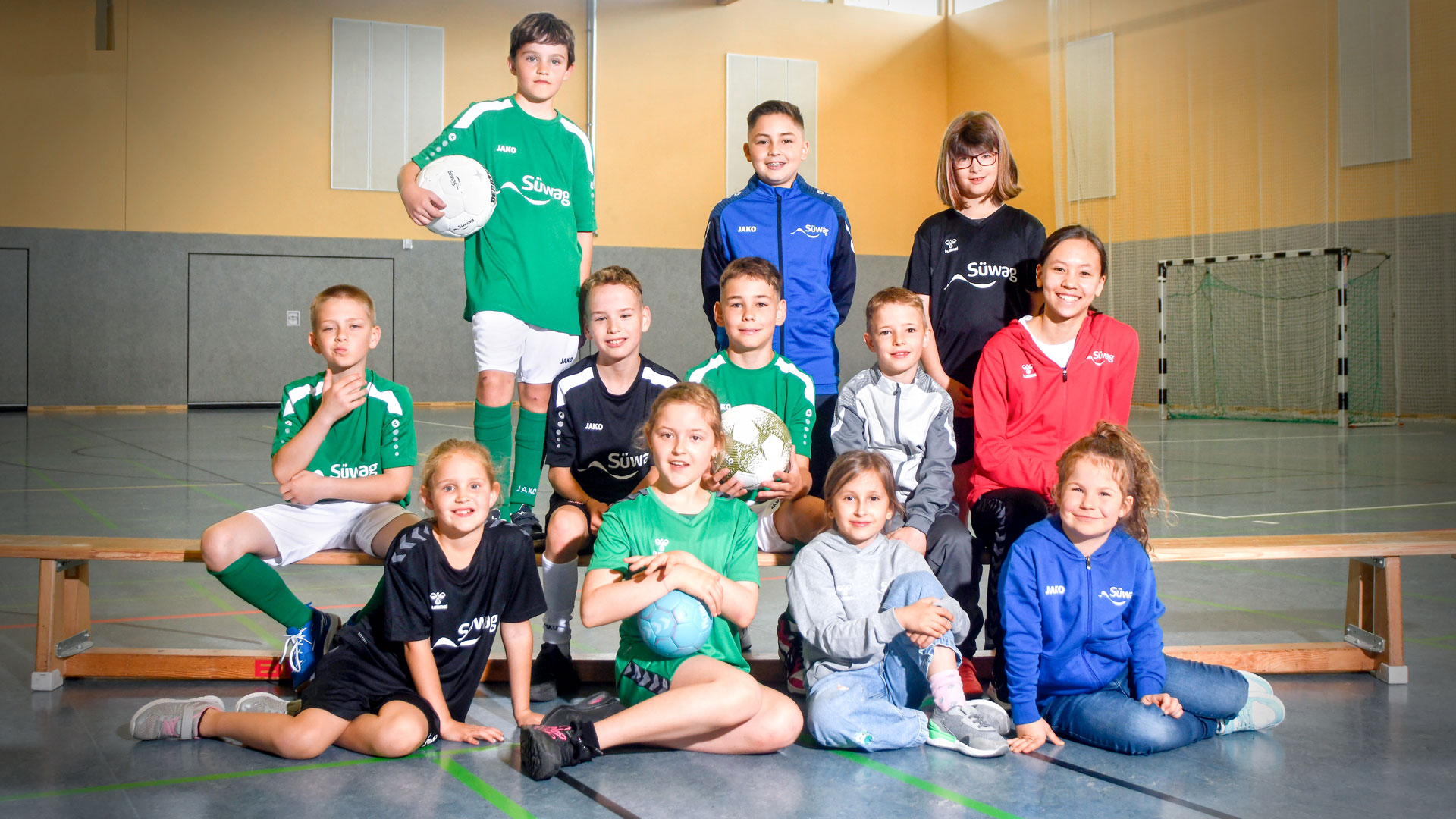 Gruppe Jugendlicher in Sportkleidung, einige mit Fußbällen, vor einer Sporthalle.