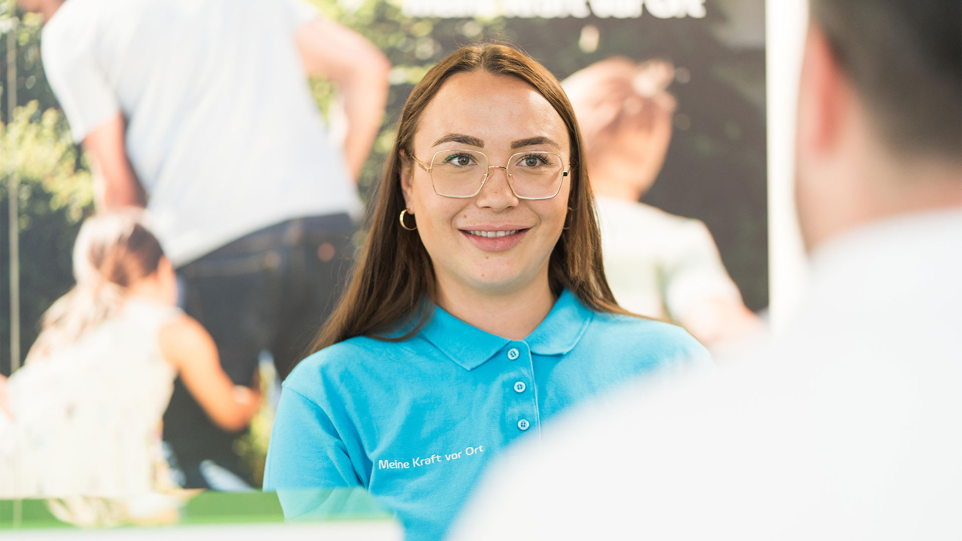 Junge Frau mit braunen Haaren und blauem Poloshirt lächelt in die Kamera.