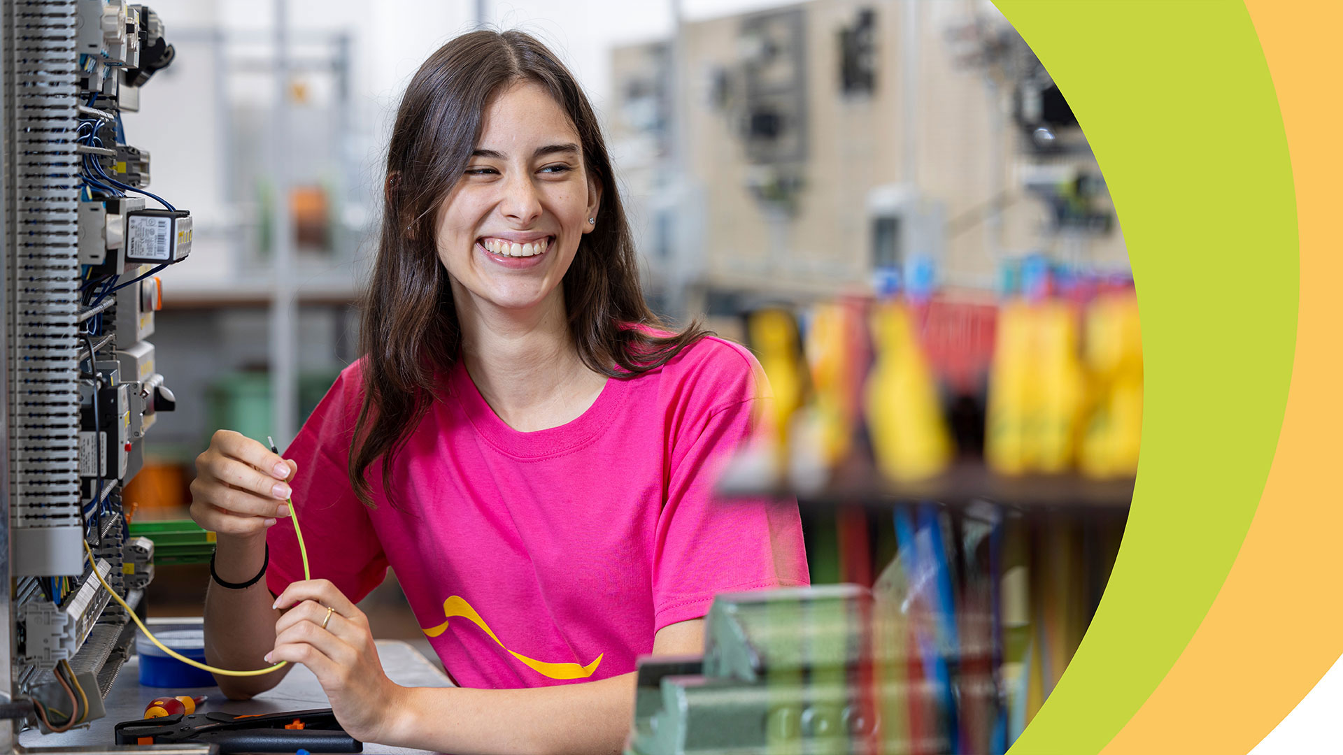 Frau mit rotem T-Shirt hält gelbes Kabel vor technischer Apparatur.