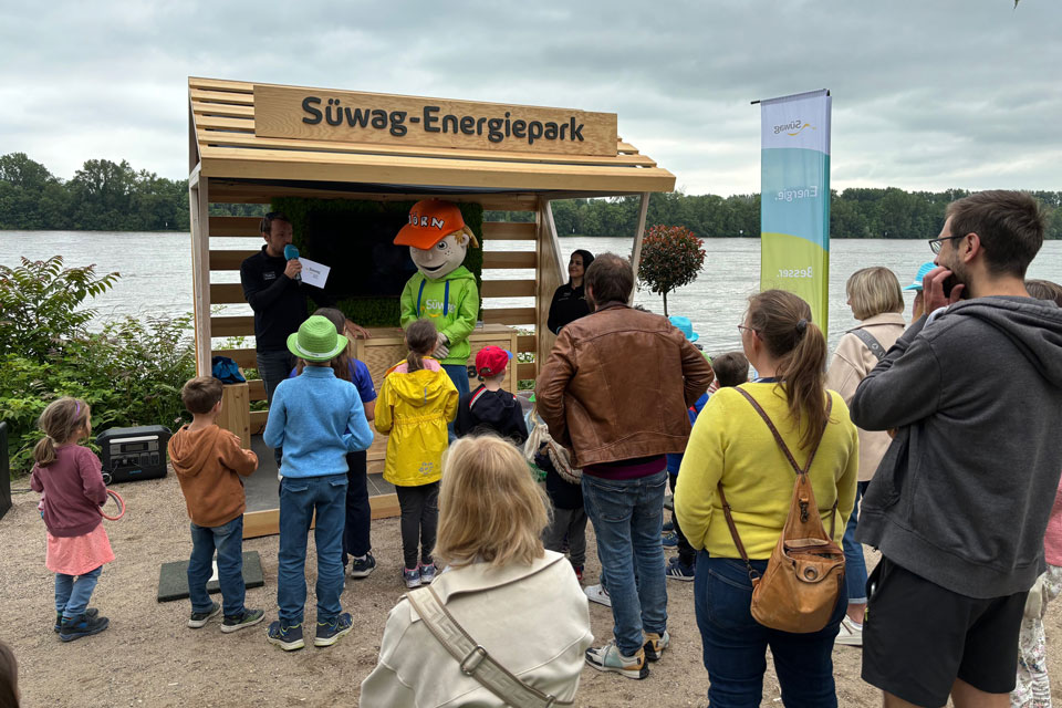 Personen vor Infostand 'Süwag Energiepark' am See.