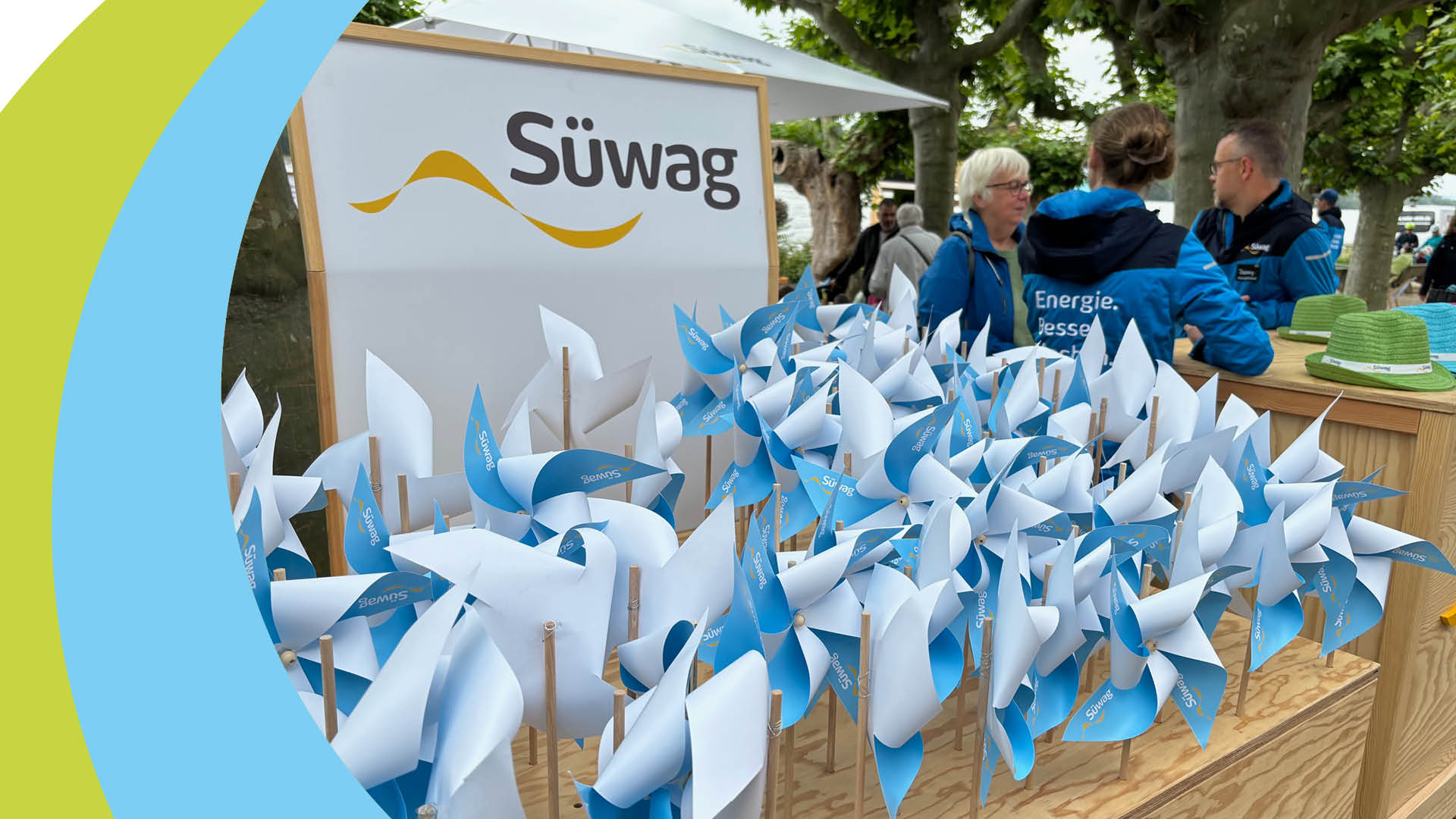 Windräder aus Papier auf Wiese, im Hintergrund Personen.