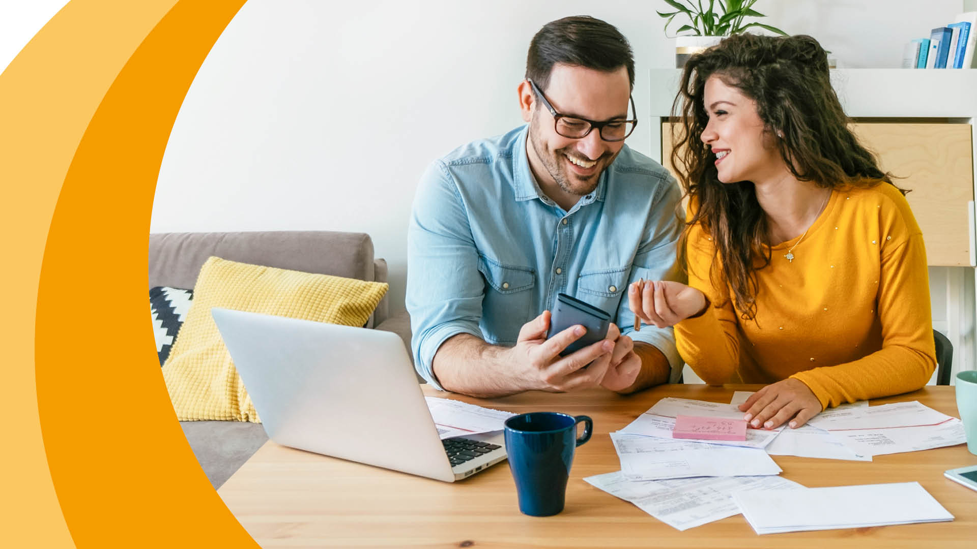 Zwei Personen sitzen an einem Tisch mit Laptop und Smartphone.