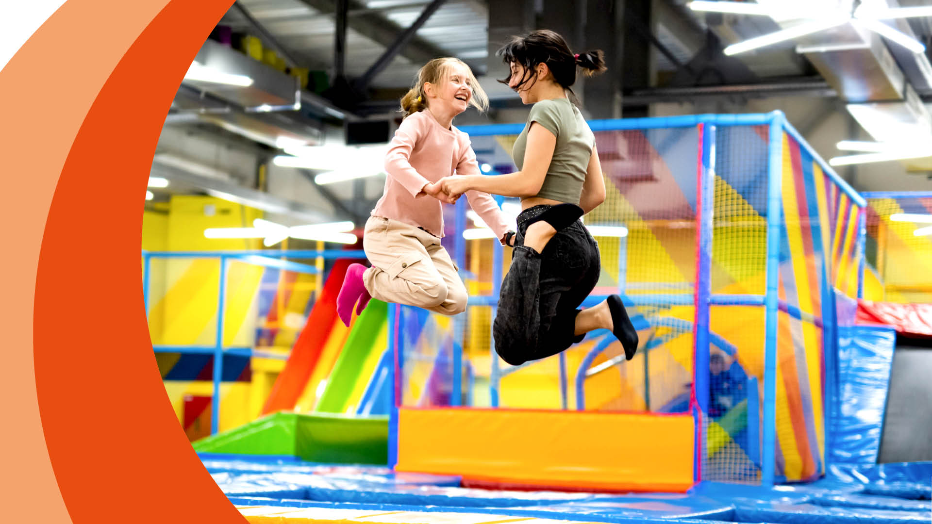 Zwei Personen springen auf einem Trampolin in einem Indoor-Spielplatz.